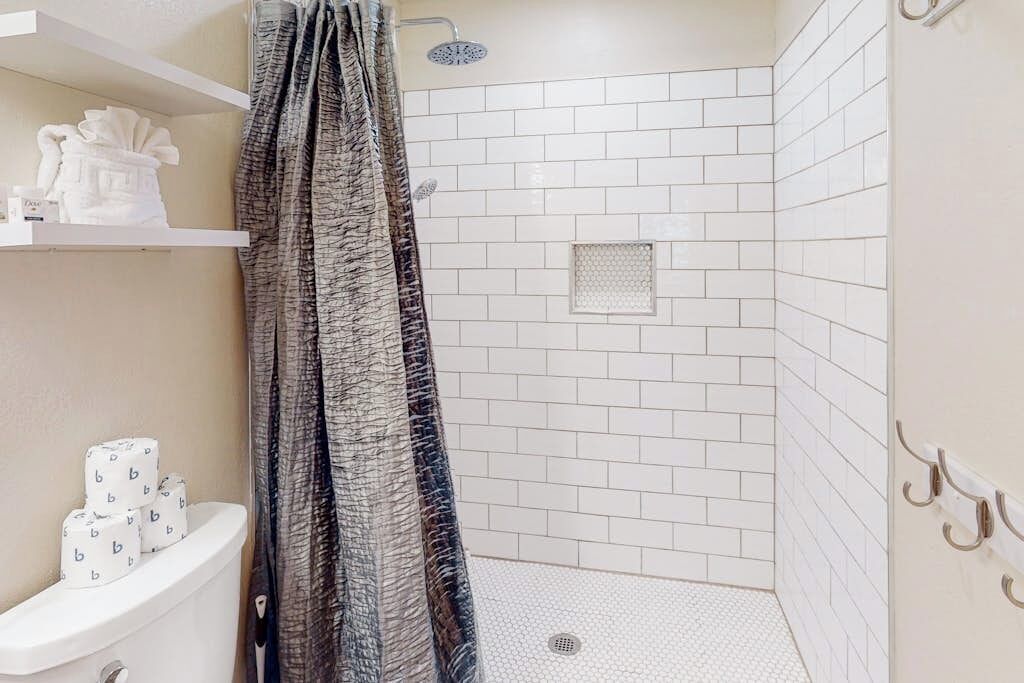 A shower with white tiles, a showerhead, and a curtain.