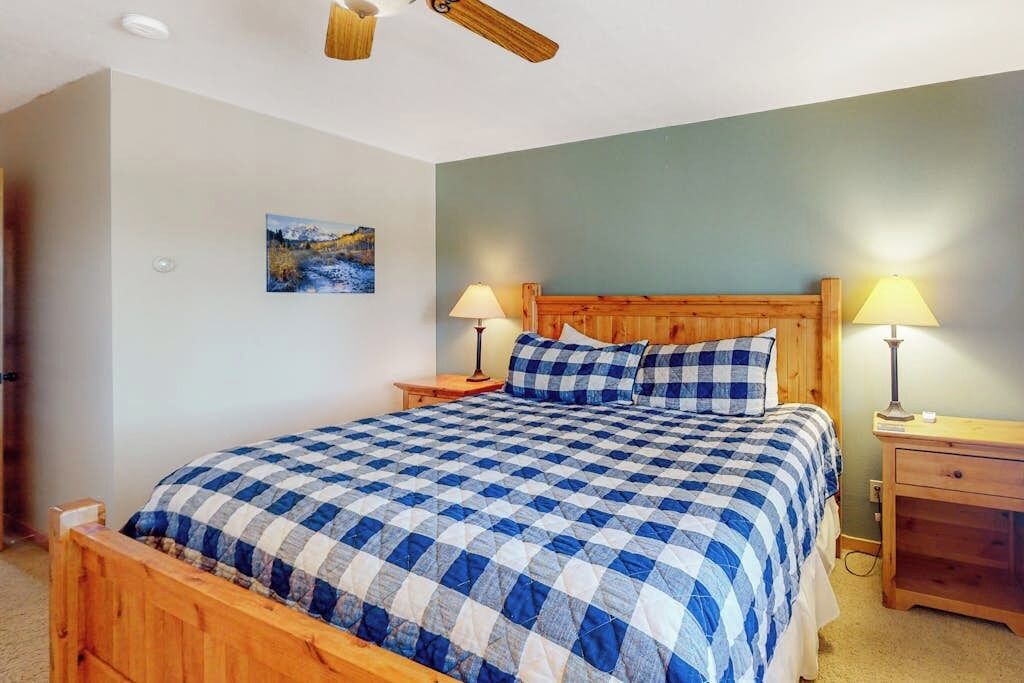 A bedroom with a wooden bed, two bedside tables, a ceiling fan, and a wall-mounted lamp.