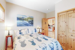 Ein Schlafzimmer mit einem Bett, einem Gemälde, einem Holzschrank und einer Küchenzeile im Hintergrund.