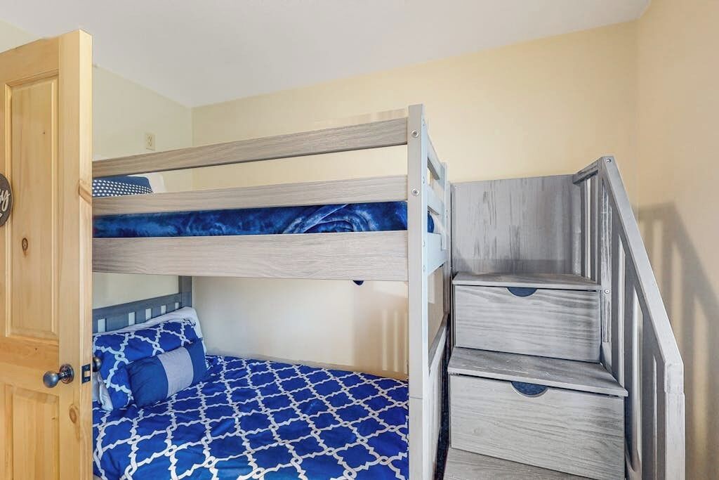 Una cama litera con una colcha azul estampada, una puerta de madera y una escalera.