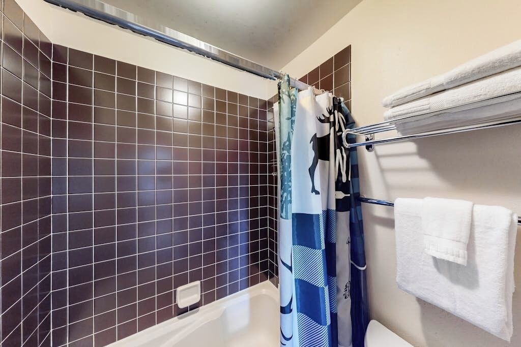 Een badkamer met donkere betegelde wanden, een douchegordijn, een handdoekhouder met een opgevouwen handdoek en een bad.