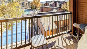 En træterrasse med gelænder, to stole og udsigt til en swimmingpool og bygninger.