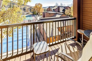 Eine Holzterrasse mit Geländer, zwei Stühlen und Blick auf einen Pool sowie Gebäude.