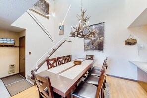 Ein Essbereich mit Holztisch, Stühlen, einer Chandelüster und einer Treppe.