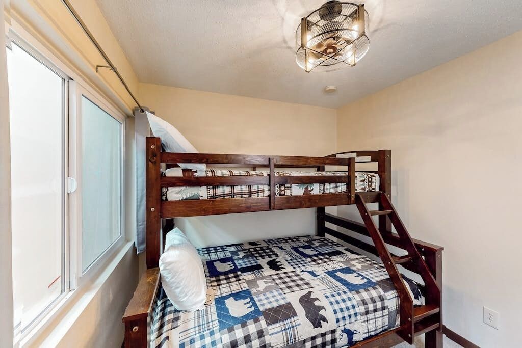 Una cama litera con colchón a cuadros, cabecera de madera y lámpara en el techo.