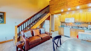 Un salón con un sofá de cuero marrón, una escalera de madera y una cocina con armarios de madera y un microondas.