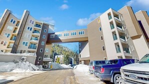 Edifício de vários andares com uma passarela central, área de estacionamento e neve no chão.