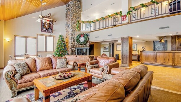 Uma sala de estar ampla com sofás de couro, lareira e varanda decorada com guirlandas festivas.