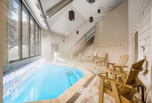 Ein Hallenbad mit großen Glaswänden, Holz-Adirondack-Stühlen und einer Treppe, die zu einer oberen Ebene führt.