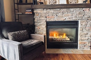 A fireplace with a stone wall, a leather sofa, and a shelf with books and decorative items. - 310 Base Camp | Condo in Granby (Granby)