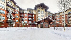 Een meerlaags gebouw met een skiweghoepigang, genaamd 'BASE CAMP ONE', met balkons en een met sneeuw bedekte ondergrond.