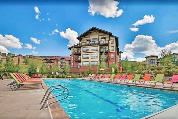 A hotel with a swimming pool, colorful lounge chairs, and a multi-story building with balconies. - 310 Base Camp | Condo in Granby (Granby)