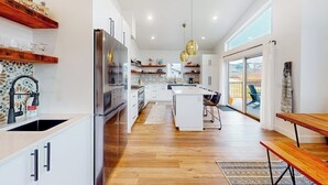 Una cucina moderna con isola centrale, pavimento in legno e illuminazione a sospensione.