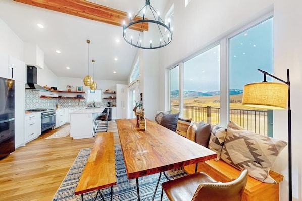 A modern kitchen with a wooden dining table, a large window with a view, and a chandelier. - Dog-friendly golf course-front home with mtn & ski views, fireplace, & balconies (Granby)