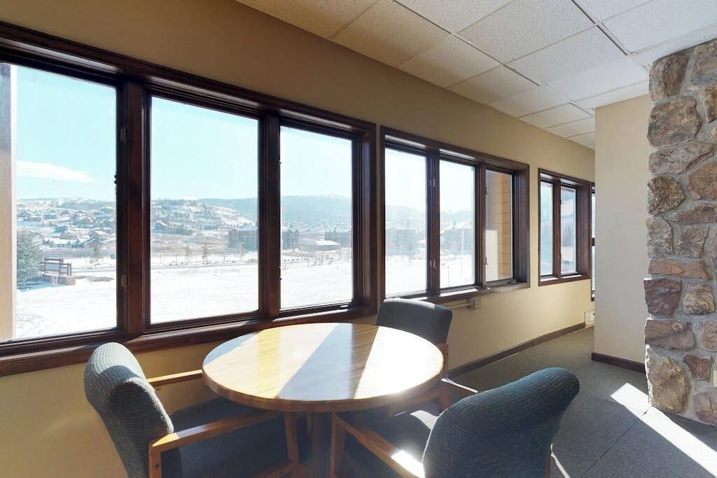 A conference room with a round table, four chairs, large windows, and a stone wall.