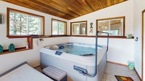 Ein Wellnessraum mit Whirlpool, Holzboden, großen Fenstern und einer Sitzbank.