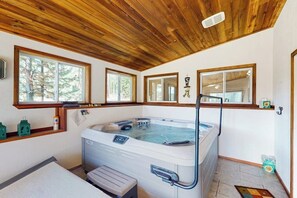Una stanza spa con vasca idromassaggio, soffitto in legno, ampie finestre e una panca.