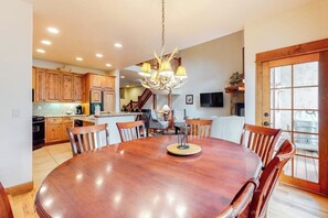 A dining area with a wooden table and chairs, a chandelier, and a view of the kitchen and living room. - Walk-to-Lift Townhome w/Fireplace, W/D, Shared Hot Tubs, Pool, and Firepit (Steamboat Springs)