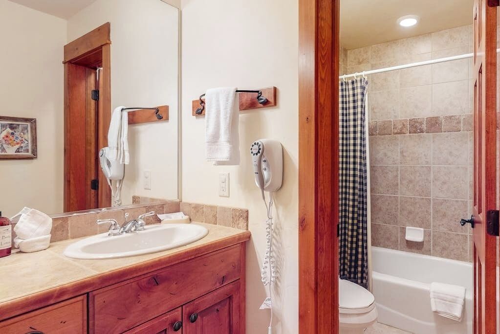A bathroom with a sink, mirror, hairdryer, and a shower area.