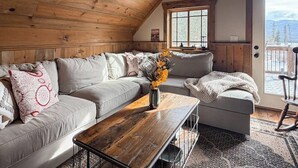 Un salon chaleureux avec un plafond en bois, un canapé, une table basse et une vue sur l’extérieur.