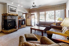 A cozy living room with a fireplace, a sofa, a coffee table, and a television. - Beautiful condo w/shared pools, hot tubs, & ski shuttle + private washer/dryer (Steamboat Springs)
