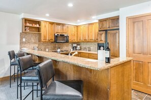 Eine Küche mit Holzausstattung, einer Arbeitsplatte aus Granit, einer Mikrowelle, einem Kühlschrank und Barhocker.