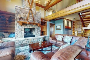 Ein gemütliches Wohnzimmer mit Kamin aus Stein, Ledersofas und einer Holztreppe.