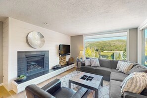 Ein modernes Wohnzimmer mit Kamin, großem Fenster und Aussicht, einer Couch und einem Couchtisch.