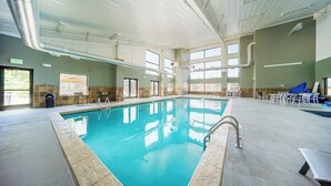 Ein Innenpool mit klarem Wasser, umgeben von einer gefliesten Liegefläche, mit Rettungsschwimmerstuhl und Sicherheitsausrüstung.