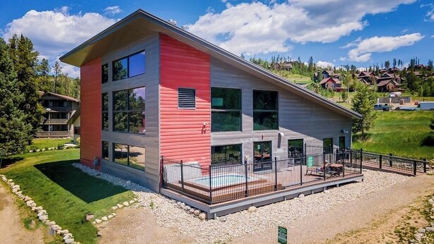 Ein modernes, zweistöckiges Gebäude mit roter und weißer Fassade, großen Fenstern und einem eingezäunten Außenbereich mit Schwimmbad.