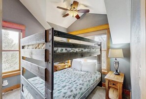 Ein Etagenbett, ein Deckenventilator, ein Nachttisch mit Lampe und ein Fenster mit Blick auf Bäume.