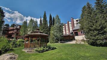 A hotel with a gazebo, lush greenery, and tall trees.