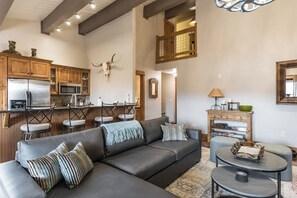 Ein modernes Wohnzimmer mit Ecksofa, Essbereich mit Stühlen, einer Küche mit Geräte und einem oberen Wohnbereich mit Blick.