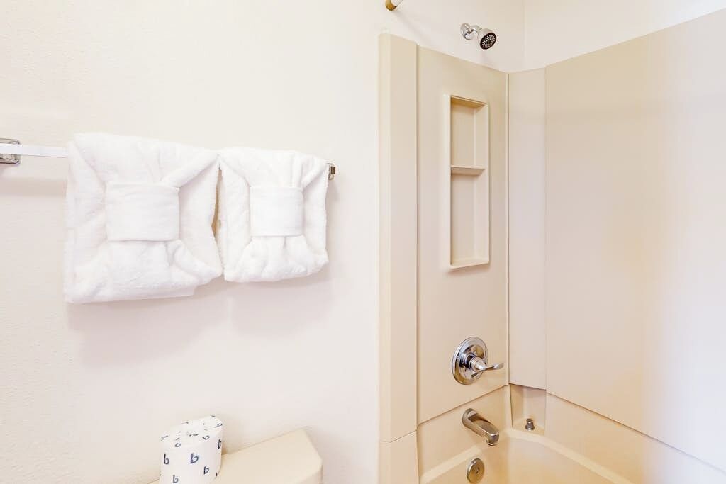 A bathroom with a toilet, a towel rack with two towels, a mirror, and a shower door.