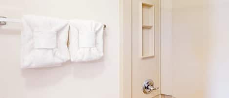 A bathroom with a toilet, a towel rack with two towels, a mirror, and a shower door.