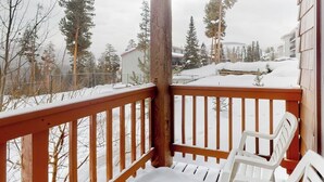 Ein hölzerner Balkon mit schneebedecktem Boden und Blick auf schneebedeckte Häuser und Bäume.