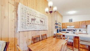 Een houten interieur met een eettafel, stoelen, een keukenhoek en een kroonluchter.