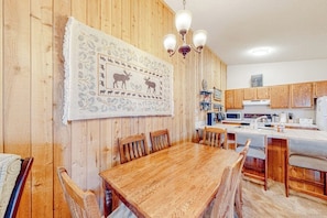 Ein Holzinterieur mit Esstisch, Stühlen, einer Küchenzeile und einer Chandelieber.