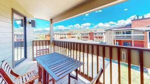 Een balkon met een tafel en stoelen, uitzicht op omliggende gebouwen en een heldere lucht.