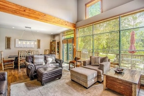 Ein geräumiges Wohnzimmer mit Ledersofas, einem Holztisch und großen Fenstern mit Jalousien.