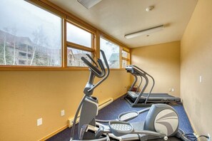 Un gimnasio con cintas de correr y máquinas elípticas, amplias ventanas y suelo alfombrado.