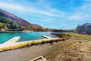 A serene outdoor pool area with a clear view of a mountain, a modern building, and a well-maintained lawn. - Mountain view condo with a wood-burning fireplace - W/D, pool, & hot tub access (Dillon)