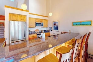 A kitchen with granite countertops, wooden cabinets, a stainless steel refrigerator, and a microwave. - Mountain view condo with a wood-burning fireplace - W/D, pool, & hot tub access (Dillon)
