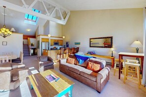 A spacious living area with a sofa, chairs, a coffee table, a dining table, and a kitchen in the background. - Mountain view condo with a wood-burning fireplace - W/D, pool, & hot tub access (Dillon)
