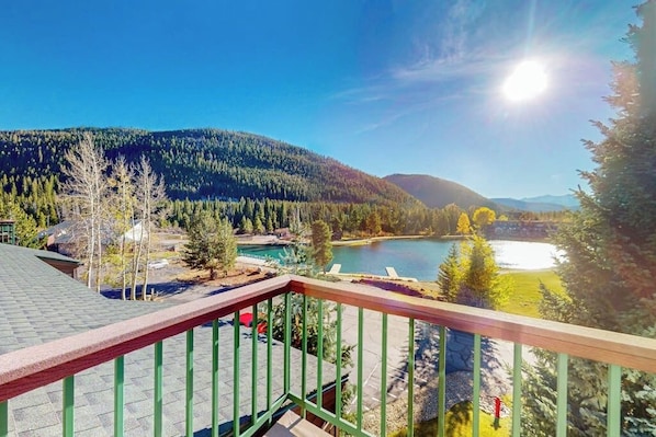 A balcony with a view of a lake, forested hills, and a clear sky. - Mountain view condo with a wood-burning fireplace - W/D, pool, & hot tub access (Dillon)