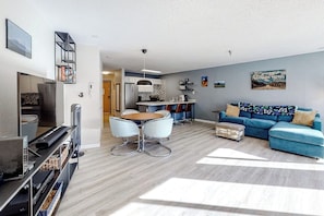 Ein modernes Wohnzimmer mit einem blauen Sofa, einem Esstisch und einer Küchenzeile im Hintergrund.