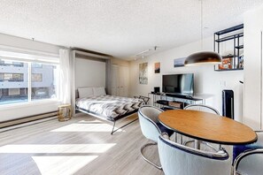 Ein modernes Hotelzimmer mit Bett, Schreibtisch, Stuhl, Fernseher und Fenster mit Blick auf Gebäude.