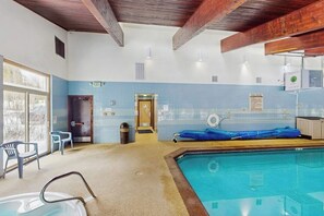 Ein Innenpool mit freier Sicht auf den Poolbereich, eine Tür, die in einen anderen Raum führt, und ein Fenster, das für natürliches Licht sorgt.