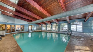 Une piscine intérieure avec des poutres en bois, de grandes fenêtres et une vue sur l’extérieur.