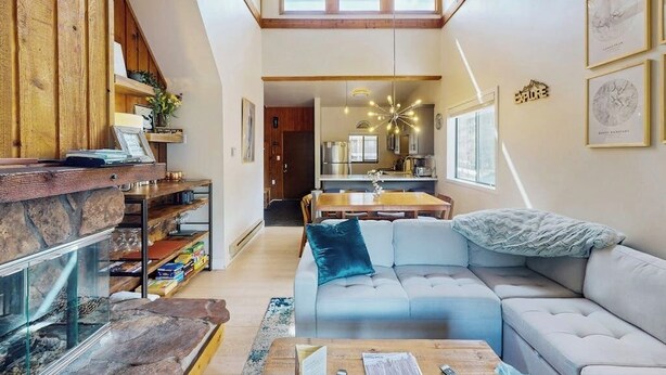 Un salon moderne avec une cheminée en pierre, un canapé bleu, une table basse en bois et une cuisine visible à travers une porte ouverte.